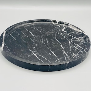 May include: A round black marble tray with white veining. The tray is perfect for serving snacks, drinks, or jewelry.