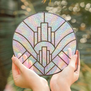 May include: A round, iridescent stained glass window with a black metal frame and chain. The design features a geometric pattern of lines and shapes, with a rainbow of colors visible through the glass.