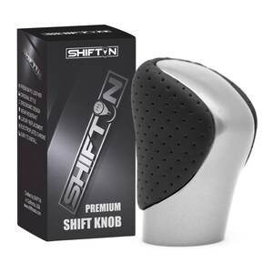 May include: A premium shift knob with a black perforated leather grip and a silver-colored base. The product is packaged in a black box with the text "SHIFTIN" and "PREMIUM SHIFT KNOB".