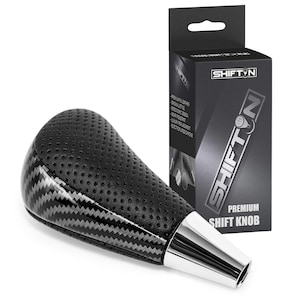 May include: Black and silver shift knob with a carbon fiber design and perforated leather grip. The shift knob has a chrome base and is packaged in a black box with the "SHIFT N" logo and product details.