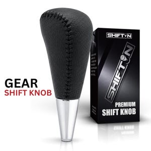 May include: A black textured leather gear shift knob with visible stitching and a polished silver metallic base. Next to it stands a black rectangular product box featuring the brand name SHIFTON and the text PREMIUM SHIFT KNOB.