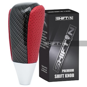May include: A premium shift knob with a carbon fiber and red leather design. The shift knob has a white base and is packaged in a black box with the "SHIFTIN" logo and "PREMIUM SHIFT KNOB" text.