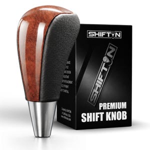 May include: A gear shift knob featuring a polished brown wood grain finish on one side and a textured black leather-like grip on the other, mounted on a silver metallic base. It is displayed next to a black box labeled SHIFTN PREMIUM SHIFT KNOB.