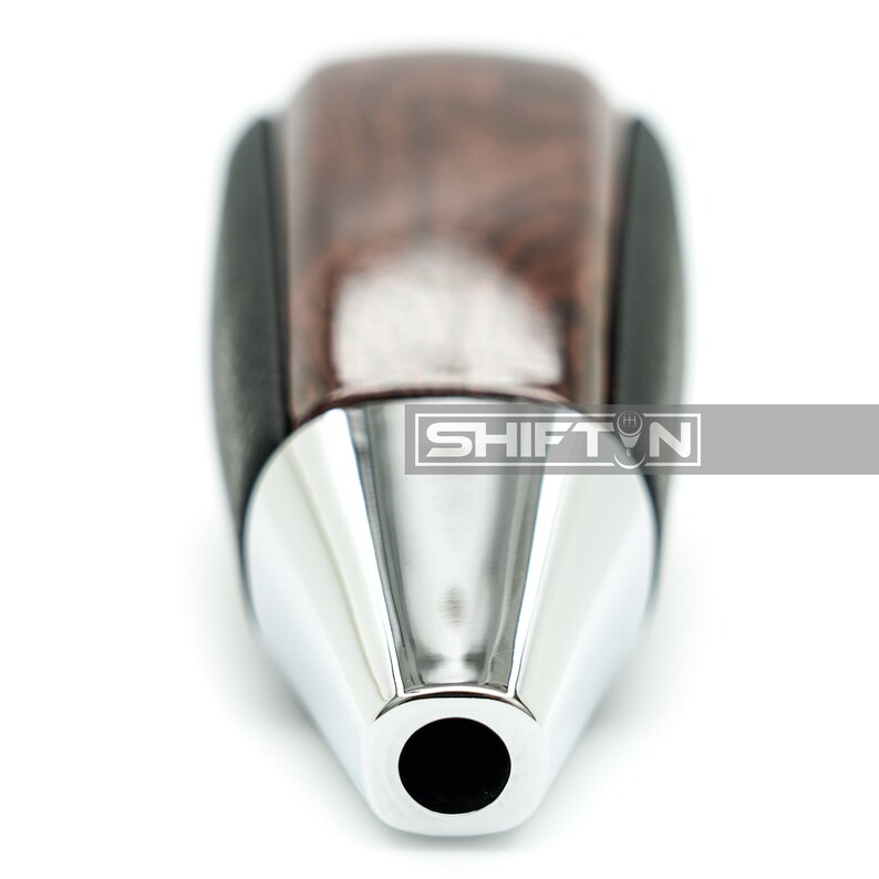 May include: A close-up of a brown wood and black leather gear shift knob with a chrome tip. The knob has a round opening at the end.