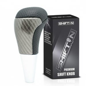 May include: A premium shift knob with a carbon fiber and gray leather design. The shift knob has a white base and is packaged in a black box with the text "SHIFTN" and "PREMIUM SHIFT KNOB".