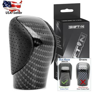 May include: A black carbon fiber shift knob with a perforated leather top. The product is displayed with its packaging, which features the brand name SHIFTIN. A comparison graphic shows the difference between dynamic quality and poor pixelated carbon fiber.