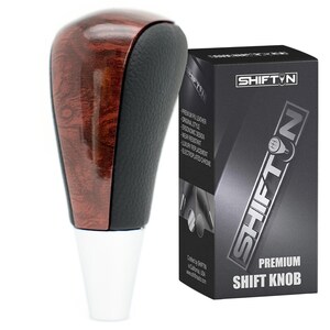 May include: A brown wood grain and black leather shift knob with a silver base. The knob is packaged in a black box with the text "SHIFTIN" and "PREMIUM SHIFT KNOB".