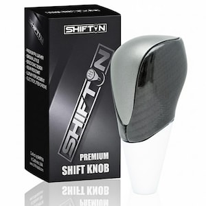 May include: A premium shift knob with a gray top and carbon fiber-style lower section. The knob is next to a black box with the "SHIFTN" logo and product details. The box reads "PREMIUM SHIFT KNOB".