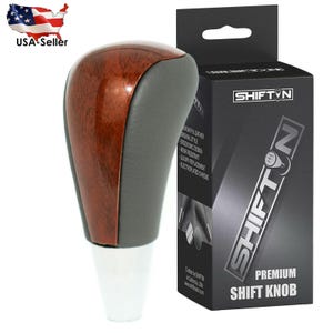 May include: A premium shift knob with a wood grain top and gray sides. The knob has a white base and is next to a black box with the text "SHIFTN" and "PREMIUM SHIFT KNOB". The box also has the text "USA-Seller".