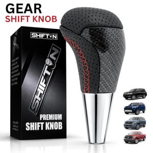 May include: A gear shift knob featuring black perforated leather, carbon fiber accents, and red stitching. The base is metallic silver. Next to it is a black box labeled GEAR SHIFT KNOB and SHIFTON, with four small images of trucks on the right side.