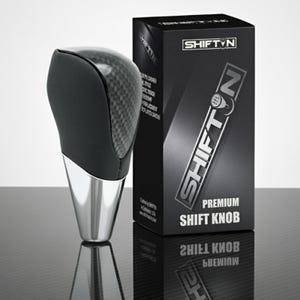 May include: A premium shift knob with a carbon fiber top and a polished chrome base. The black box next to it has the text "SHIFT N PREMIUM SHIFT KNOB". The product is designed for automotive use.