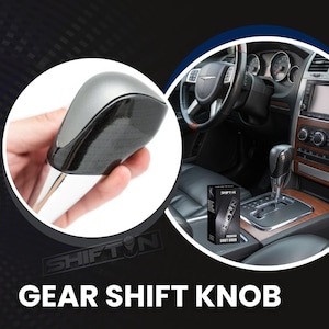 May include: A silver and black gear shift knob with a carbon fiber design. The image shows the shift knob held in a hand, with a car interior in the background. The text "SHIFT ON" and "GEAR SHIFT KNOB" are visible.