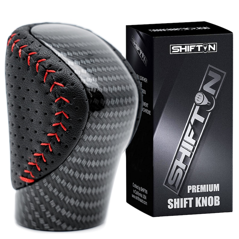 May include: A gear shift knob featuring a black carbon fibre pattern and perforated black side panels with red stitching. Next to it is a black rectangular box labelled SHIFTIN PREMIUM SHIFT KNOB with a graphic of a gear shifter and text.