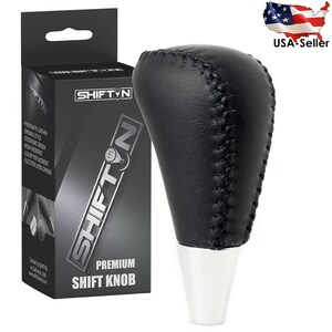 May include: A black leather shift knob with white base and stitched detailing. The product is packaged in a black box with the brand name SHIFTYN and the words "PREMIUM SHIFT KNOB".