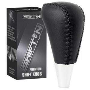 May include: A black leather shift knob with white base and black stitching. The shift knob is next to a black box with the text "SHIFTN" and "PREMIUM SHIFT KNOB". The box also lists features like "PREMIUM PU LEATHER" and "ERGONOMIC DESIGN".