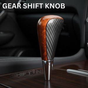 May include: Gear shift knob with a wood grain and carbon fiber design. The top of the knob is a dark wood grain, transitioning to a carbon fiber pattern. The base is a shiny silver color. The text "GEAR SHIFT KNOB" is at the top.