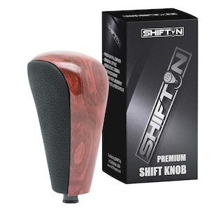 May include: A premium shift knob with a wood grain finish and black accents. The knob is next to a black box with the text "SHIFT N" and "PREMIUM SHIFT KNOB". The box also lists features like ergonomic design and replacement chrome.