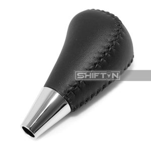 May include: A black leather shift knob with a silver base. The shift knob has a stitched design and the text "SHIFT N" is visible on the side. The knob is designed for a vehicle's gear shift.