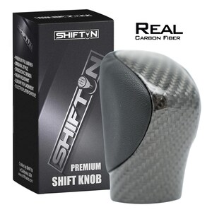 May include: A premium shift knob with a carbon fiber design and a black leather top. The product is packaged in a black box with the brand name "SHIFTIN" and the text "REAL CARBON FIBER". The box also lists features like "premium PU leather" and "ergonomic design".