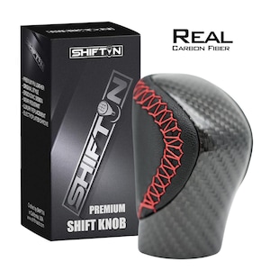 May include: A premium shift knob with a carbon fiber design and red stitching. The product is packaged in a black box with the "SHIFTN" logo and product details. The text "REAL CARBON FIBER" is also visible.