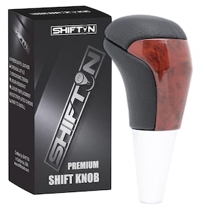 May include: A premium shift knob with a black leather top and a wood grain accent. The shift knob has a white base and is packaged in a black box with the "SHIFT N" logo and product details.