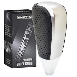 May include: A premium shift knob with a black, perforated grip and a silver metallic top. The product is next to a black box with the "SHIFTN" logo and product details. The shift knob has a white base.