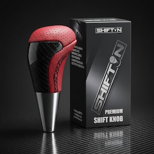 May include: A premium shift knob with a red perforated leather top and carbon fiber accents. The shift knob has a black and silver base and is next to a black box with the text "SHIFTN PREMIUM SHIFT KNOB".