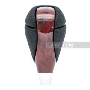 May include: A car gear shift knob with a wood grain finish and black leather top. The bottom is white. The text "SHIFTN" is visible on the side.