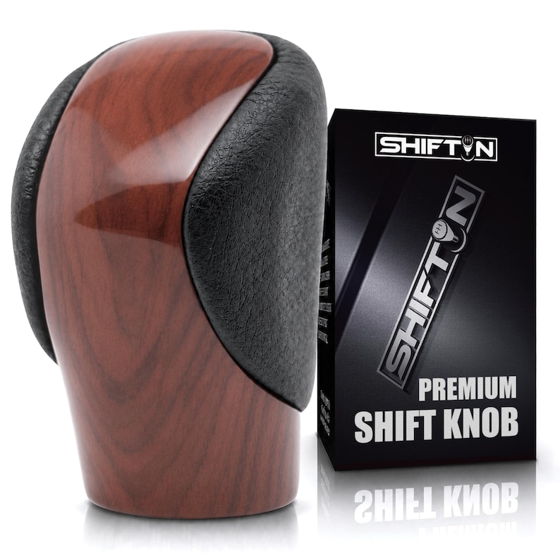 May include: A gear shift knob featuring a polished brown wood grain centre panel flanked by textured black side grips. Next to the knob is a black rectangular box with the text SHIFTN and PREMIUM SHIFT KNOB printed in white lettering.