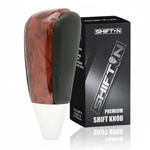 May include: A premium shift knob with a wood grain top and black leather grip. The shift knob has a white base and is next to a black box with the text "SHIFT N" and "PREMIUM SHIFT KNOB".