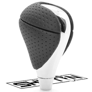 May include: A car gear shift knob with a black, perforated leather top and a white, glossy base. The design features a curved shape with a chrome accent. The bottom of the knob has a white, cylindrical base. The image is set against a white background.