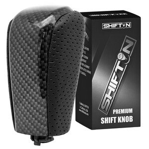 May include: A black and gray shift knob with a carbon fiber weave pattern and perforated leather accents. The shift knob is next to a black box with the text "SHIFT N" and "PREMIUM SHIFT KNOB".