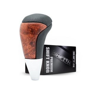 May include: A premium shift knob with a black leather top and wood grain side panel. The base is white. A black box with the text "SHIFT N PREMIUM SHIFT KNOB" is next to the knob.