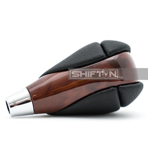 May include: A car gear shift knob with a wood grain finish and black leather accents. The shift knob has a chrome tip and the word "SHIFT N" is printed on the side.