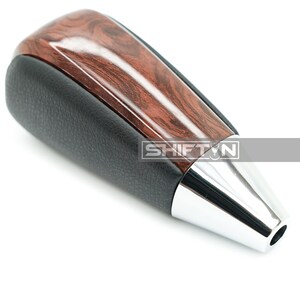 May include: A car shift knob with a wood grain top, black leather sides, and a chrome base. The text "SHIFT N" is visible on the side of the knob.