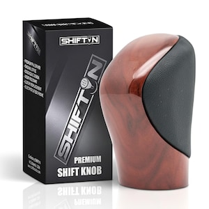 May include: A premium shift knob with a wood grain finish and black leather accents. The product is packaged in a black box with the "SHIFT N" logo and product information. The text "PREMIUM SHIFT KNOB" is also visible.