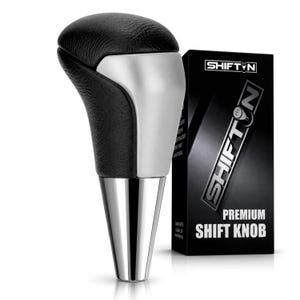 May include: A black textured gear shift knob with a silver metallic accent and a tapered chrome base. Next to it stands a black rectangular box labeled SHIFTN PREMIUM SHIFT KNOB with a graphic of a gear pattern inside the letter N.