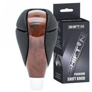 May include: A premium shift knob with a black leather top and a wood-grain finish. The knob has a white base and is next to a black box with the text "SHIFT N PREMIUM SHIFT KNOB".