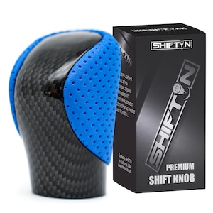 May include: A car gear shift knob featuring a black carbon fibre pattern on the top and sides, accented by bright blue perforated side panels. Next to it stands a black rectangular product box labelled SHIFTN PREMIUM SHIFT KNOB.