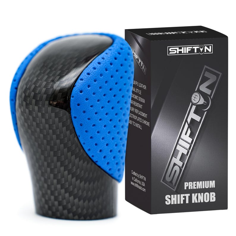 May include: A car gear shift knob featuring a black carbon fibre pattern on the top and sides, accented by bright blue perforated side panels. Next to it stands a black rectangular product box labelled SHIFTN PREMIUM SHIFT KNOB.