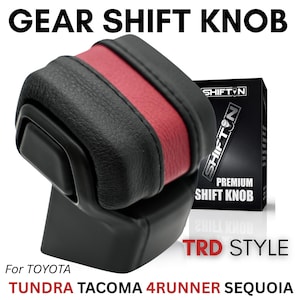 May include: A black and red gear shift knob with a textured finish and a side button. The product is labeled as a premium shift knob for Toyota Tundra, Tacoma, 4Runner, and Sequoia vehicles, featuring TRD style branding and a SHIFTON box.