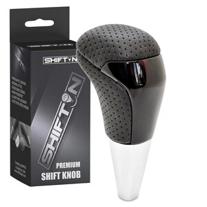 May include: A black and silver premium shift knob with a perforated leather top and a shiny chrome base. The product is packaged in a black box with the "SHIFT N" logo and product details. The text "PREMIUM SHIFT KNOB" is also visible.