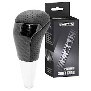 May include: A black and gray shift knob with a carbon fiber design and a perforated top. The product is packaged in a black box with the text "SHIFTN" and "PREMIUM SHIFT KNOB".