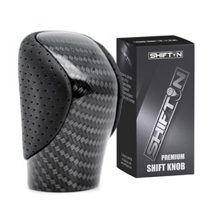 May include: A premium shift knob with a carbon fiber weave design and black perforated leather. The product is packaged in a black box with the "SHIFTN" logo and product information.