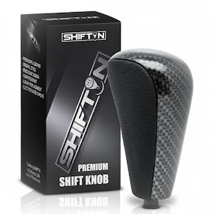May include: A black and gray shift knob with a carbon fiber design, next to a black box with the text "SHIFT N" and "PREMIUM SHIFT KNOB". The box also lists features like "premium PU leather" and "ergonomic design".