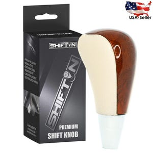 May include: A premium shift knob with a wood grain top and cream-colored side. The knob is labeled "SHIFTN" and "PREMIUM SHIFT KNOB" on the packaging. The box also lists features like "original style" and "wear resistant".