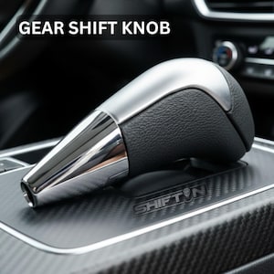 May include: A gear shift knob with a chrome and black leather design. The top of the knob is black leather, and the bottom is chrome. The text "GEAR SHIFT KNOB" is at the top of the image.