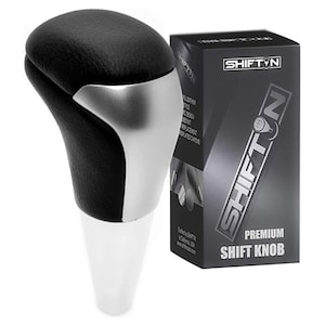 May include: A black and silver shift knob with a white base. The shift knob has a leather-like texture and a metallic silver accent. The product is packaged in a black box with the text "SHIFT N" and "PREMIUM SHIFT KNOB".