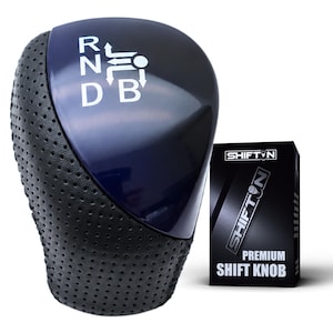 May include: A dark blue gear shift knob with a perforated black leather-like grip and a white gear pattern displaying R, N, D, and B. Next to it is a black rectangular box labeled SHIFTON PREMIUM SHIFT KNOB with a graphic of the product.