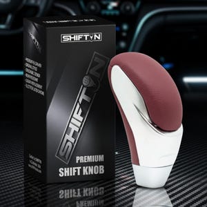 May include: A premium shift knob with a burgundy leather top and chrome accents. The product is displayed next to a black box with the "SHIFTN" logo and product details. The text "PREMIUM SHIFT KNOB" is visible on the box.